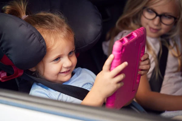 車の旅で後部座席でデジタルタブレットを見て2人の若い女の子 — ストック写真