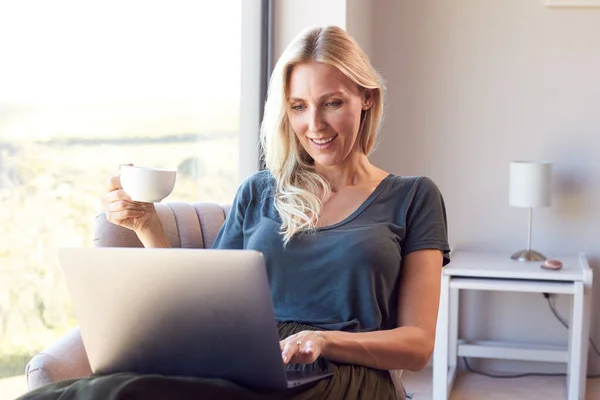 Kvinna Avkopplande Stolen Genom Fönstret Hemma Använda Laptop Dricka Kaffe — Stockfoto