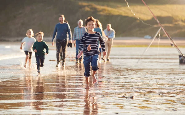 在冬季海滩度假时 多代家庭沿着海滨散步 孩子们在前方奔跑 — 图库照片