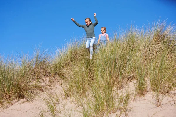 两个女孩在海滩度假时玩乐滑落沙丘 — 图库照片