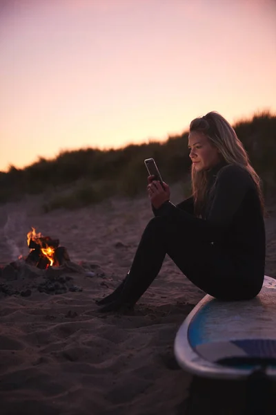 Mujer Sentada Tabla Surf Junto Fuego Del Campamento Playa Usando — Foto de Stock