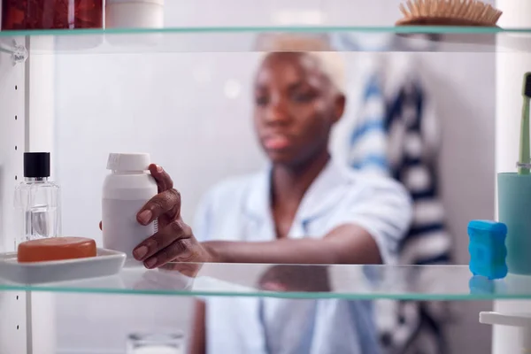 容器から薬を飲む若い女性の浴室のキャビネットを通して見る — ストック写真