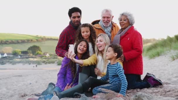 Wielopokoleniowa Rodzina Siedząca Wokół Ognia Zimowej Plaży Robiąca Selfie Telefonem — Wideo stockowe