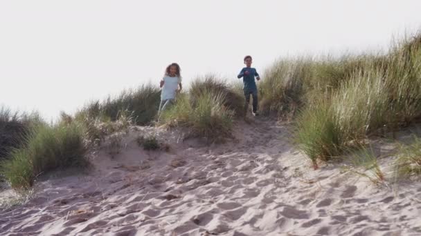 2人の子供が冬のビーチ休暇で砂丘を走ったりジャンプしたり スローモーションで撮影 — ストック動画