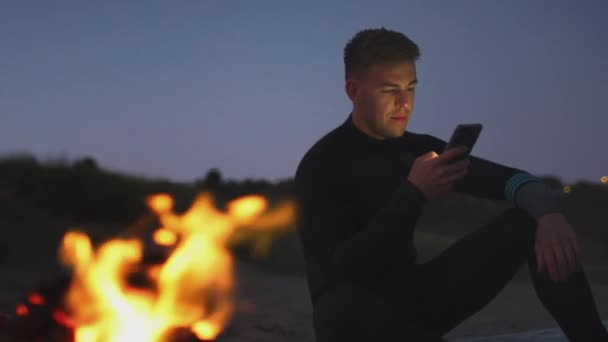 Man Sommarsemester Sitter Vid Lägereld Stranden Med Mobiltelefon Som Solen — Stockvideo