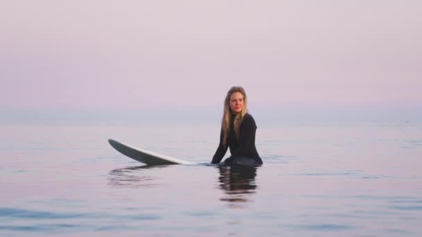 波が彼女の周りを破るようにサーフボード上に浮かんでいるウェットスーツを身に着けている女性サーファー スローモーションで撮影 — ストック動画