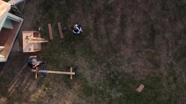 一緒に木製の夏の家を構築庭で2人の大工のドローン空中撮影 — ストック動画