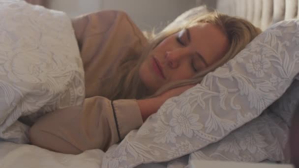 ベッドサイドテーブルの上で携帯電話上で実行されている睡眠データアプリとベッドで寝る女性 スローモーションで撮影 — ストック動画