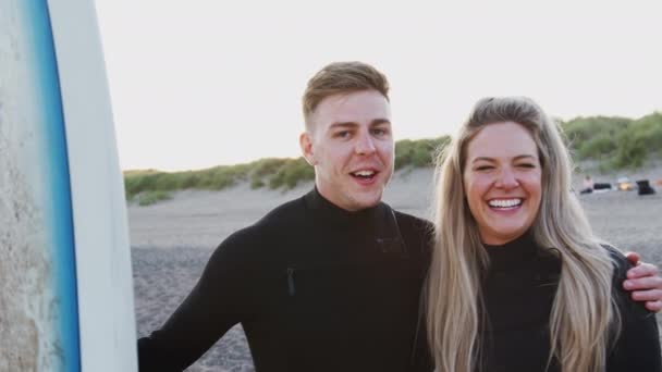 夏休みにサーフボードを持って日没時にビーチに立って笑顔の若いカップルの肖像画 スローモーションで撮影 — ストック動画