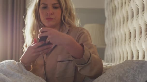 女人在床上设置睡眠数据应用程序在床头柜的手机上运行 慢动作射击 — 图库视频影像