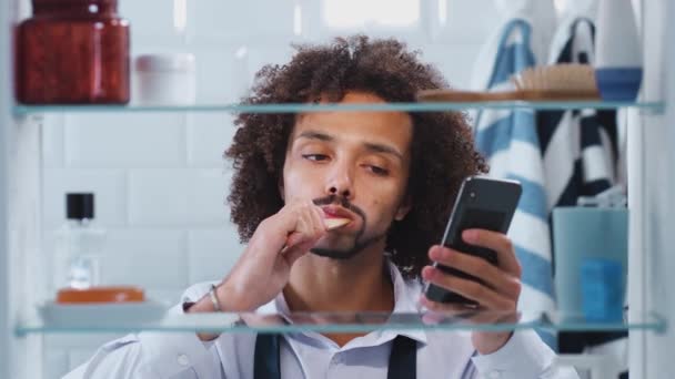 Visa Genom Badrumsskåp Ung Affärsman Borsta Tänder Och Kontrollera Meddelanden — Stockvideo