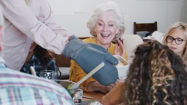 自宅でテーブルの周りに座っている世代の家族に食事を提供する母親 スローモーションで撮影 — ストック動画