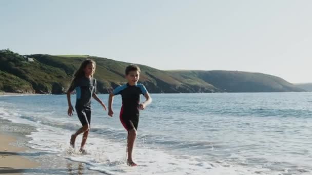 Two Children Wearing Wetsuits Running Waves Summer Beach Vacation Shot — Stock Video