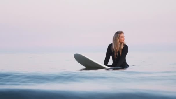 波が彼女の周りを破るようにサーフボード上に浮かんでいるウェットスーツを身に着けている女性サーファー スローモーションで撮影 — ストック動画