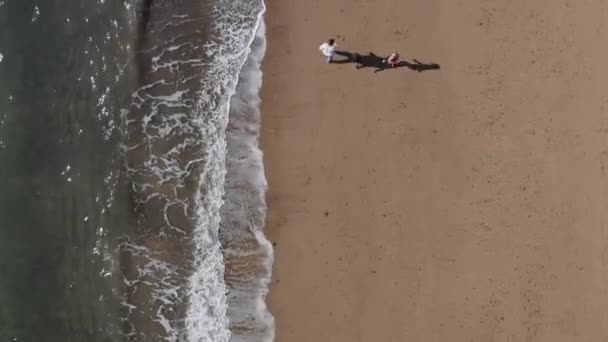 波を砕いて海岸線を歩いている子供たちと父親のドローンショット — ストック動画