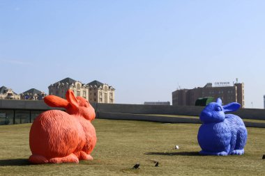 Parktaki yeşil çimlerin üzerinde kırmızı ve mavi iki büyük heykel tavşanı