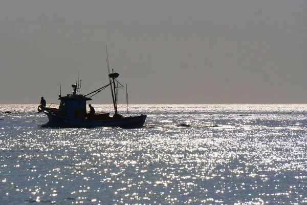  Atlantik Okyanusu 'nda bir gün. Balıkçı teknesinin silueti ve dalgaların üzerindeki parlak ışık. Çok güneş alıyor.                              