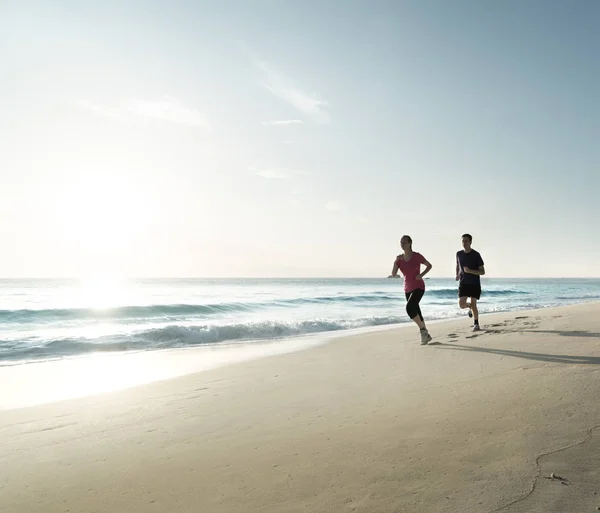 Mies ja nainen juoksemassa trooppisella rannalla auringonlaskun aikaan — kuvapankkivalokuva