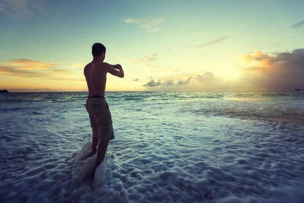 Homem tirando fotos do pôr do sol na praia tropical por smartphone — Fotografia de Stock