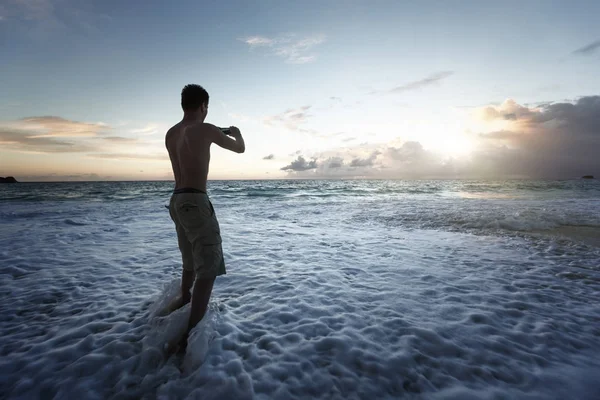 Homem tirando fotos do pôr do sol na praia tropical por smartphone — Fotografia de Stock