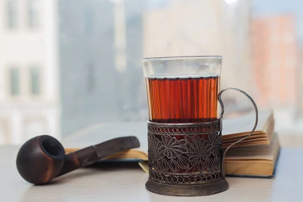 Fincanda bir bardak çay, yanında kitap ve pipo.