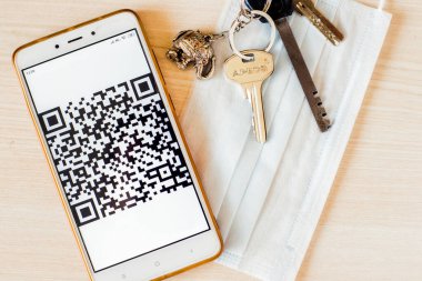 Koronavirüs salgını sırasında arka planda elektronik kartı, anahtarı ve tıbbi maskesi olan bir telefon.