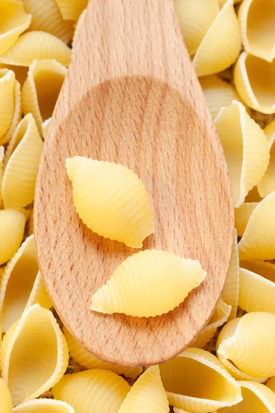 Conchiglie Rigate Pasta en fondo de cuchara de madera . Fotos De Stock