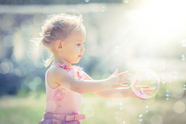 一个小女孩在夏日公园里捕捉肥皂泡沫 图库图片