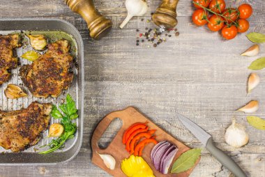 Kızarmış et dilimleri pan, domates yeşil soğan sarımsak biber, lezzetli yemekler. Ahşap masa, arka plan üzerinde bıçak çatal.