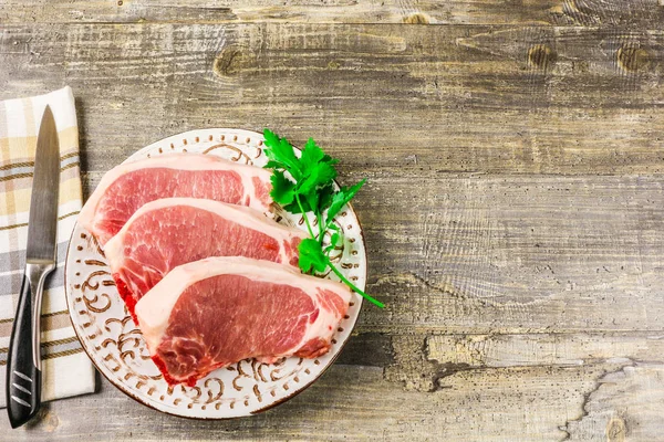 White plate raw sliced meat on wooden table, top view. Food, a knife, branches of greens Stock Photo