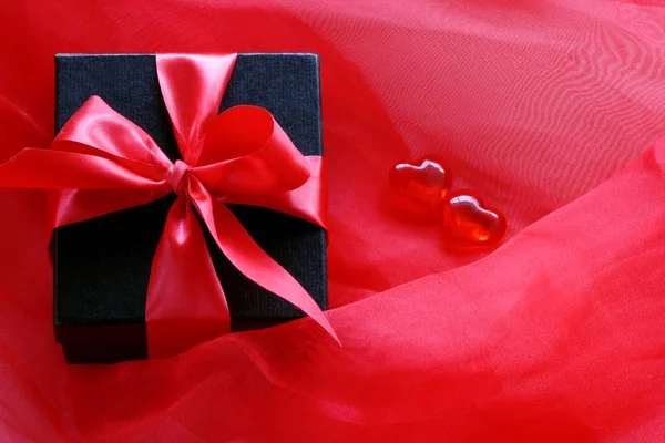 Schwarze Geschenkbox mit roter Schleife auf scharlachrotem transparentem Stoff — Stockfoto