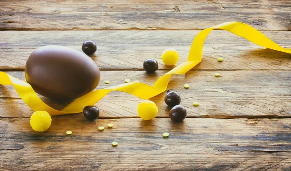 Пасхальное шоколадное яйцо, шоколадные драже, желтая шелковая лента — стоковое фото