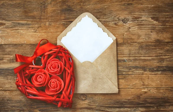 Coração de vime vermelho com rosas, envelope com nota em branco — Fotografia de Stock