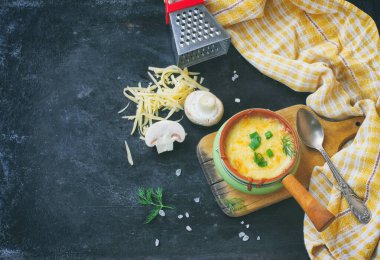 Mantarlı fırında jülyen, soğan ve peynir siyah masada, tahta tahtada, ekose havlu, peynir rendesi, üst manzara.