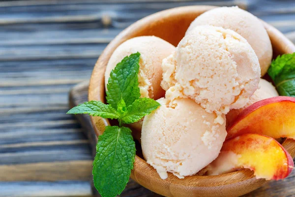 Balls peach ice cream in a wooden bowl closeup.