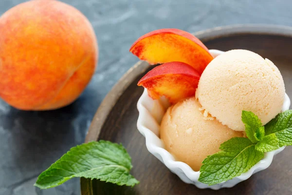 Peach ice cream and peach slices in a white bowl.