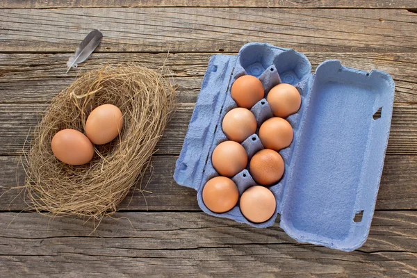 Eier im Nest und Pappverpackung auf Holzgrund — Stockfoto