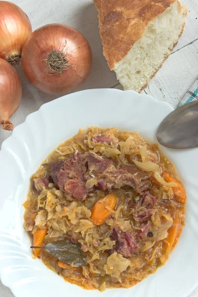 Sauerkraut mit geräuchertem Schweinefleisch im Teller auf weißem Tisch — Stockfoto