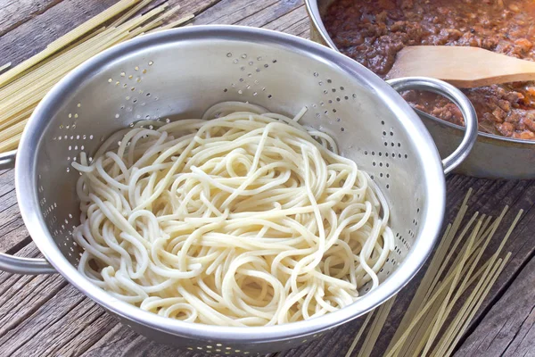 Spaghetti  pasta in strainer and bolognese sauce on table — Stock Photo, Image