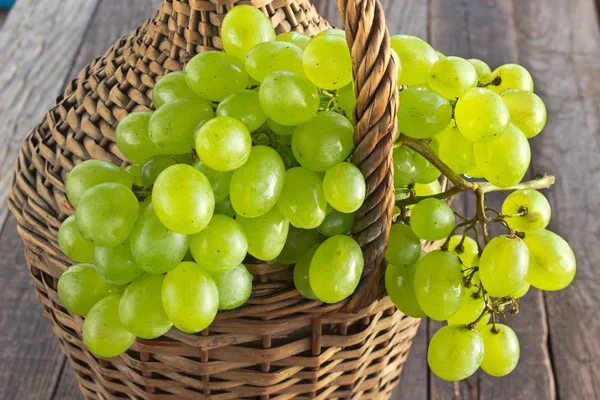 White grape with on old wicker wrapped glass bottle on wooden ta — Stock Photo, Image