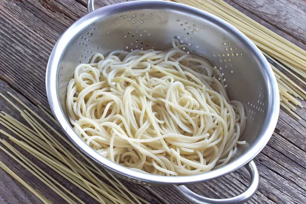 Ahşap masa üstünde süzgeç pişmiş spagetti makarna — Stok fotoğraf