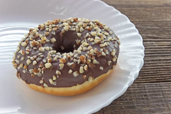 Donut med choklad och hackade mandlar i tallriken på bordet — Stockfoto