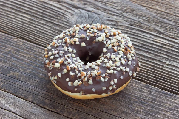 Donut mit Schokolade und gehackten Mandeln auf Holztisch — Stockfoto