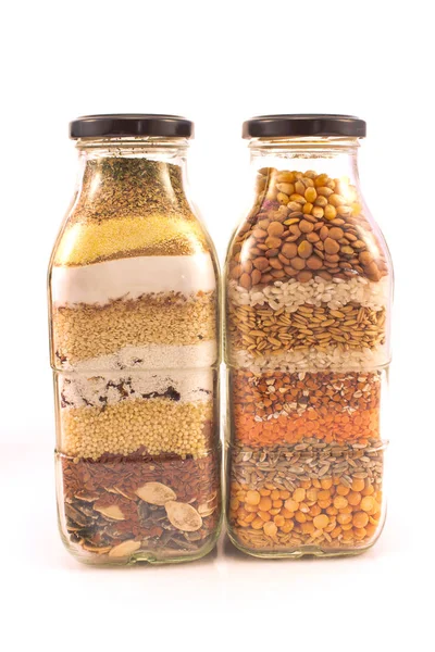Decoratieve glazen flessen met verschillende zaden geïsoleerd op wit — Stockfoto