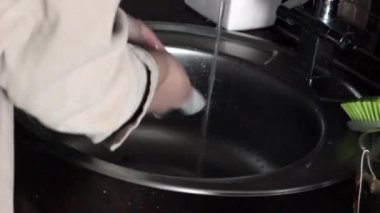 Bir kadın evde lavaboyu yıkıyor.