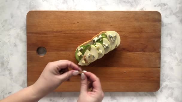 Женщина кладет орех на брускетту с авокадо и грушей — стоковое видео