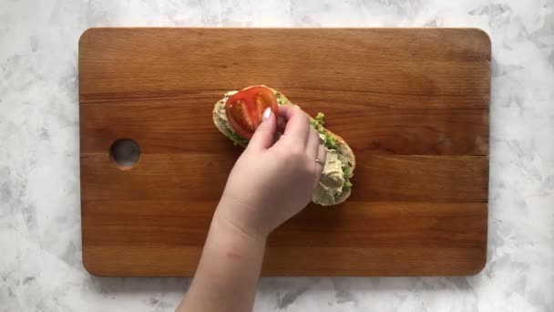 Een vrouw bereidt een heerlijke bruschetta van tomaten, avocado en hummus — Stockvideo