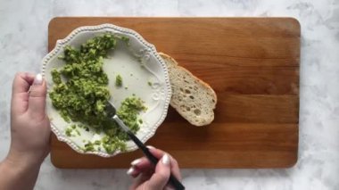 Bir kadın kızarmış ekmeğin üzerinde avokado püresi servis ediyor.