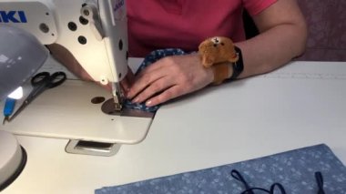 Bir kadın mavi izli bir kumaştan maske dikiyor.