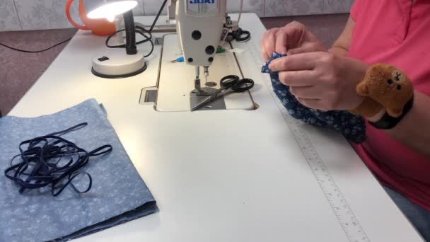 Una mujer cose una máscara de un tejido con un estampado azul — Vídeos de Stock